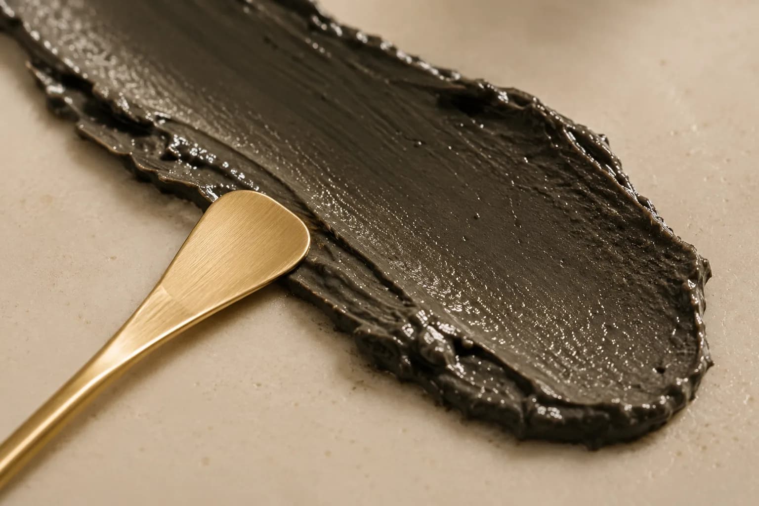 A smear of the Lamsa formula, glossy and mineral-dense, with a gold spatula